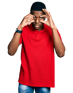 Young african american man wearing casual red t shirt trying to open eyes with fingers, sleepy and tired for morning fatigue