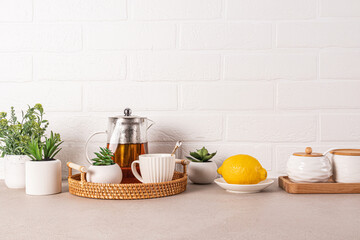 Beautiful kitchen background with glass teapot of fragrant tea, cup, lemon on wicker tray. Front...