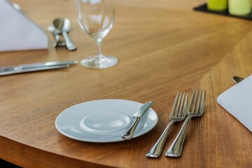 Plate, fork, spoon, cutlery, dining table on a wooden table in a restaurant, closeup shot