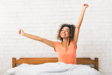 African-american woman stretching, sitting on bed in morning