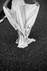 Vertical shot of a woman in a white silk dress walking on the road