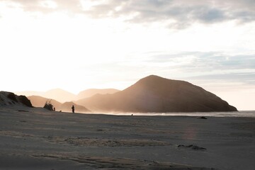 Sandy beach with misty mountains and a person silhouette in the background