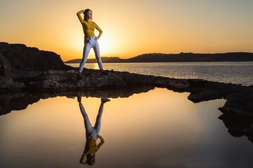 Woman standing on a rock on the seaside at sunset