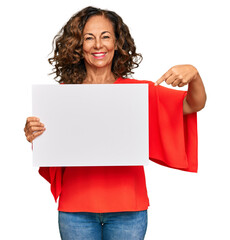 Middle age hispanic woman holding blank empty banner smiling happy pointing with hand and finger