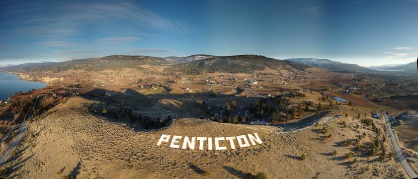 Aerial panoramic shot of the rocky mountains with a huge text 'penticton' on it
