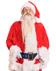 Old senior man with grey hair and long beard wearing traditional santa claus costume puffing cheeks with funny face. mouth inflated with air, crazy expression.