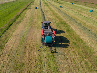 Schwarzer Treker oder Traktor mit einer roten Stroh Festkammerpresse bei der Strohernte auf einem gemähten Feld - 775039193