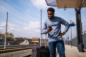Angry man with a suitcase and mobile phone  standing on a railway  station. - 775039197