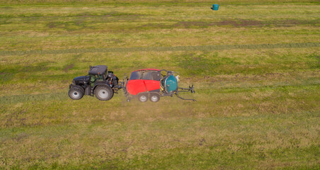 Schwarzer Treker oder Traktor mit einer roten Stroh Festkammerpresse bei der Strohernte auf einem gemähten Feld - 775039345
