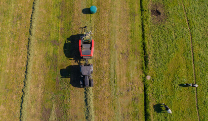 Schwarzer Treker oder Traktor mit einer roten Stroh Festkammerpresse bei der Strohernte auf einem gemähten Feld - 775039367