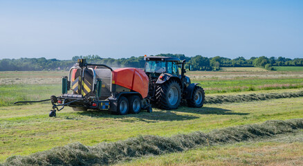 Schwarzer Treker oder Traktor mit einer roten Stroh Festkammerpresse bei der Strohernte auf einem gemähten Feld - 775039381