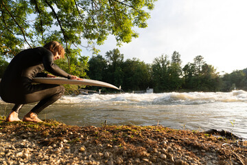 A young surfer kneels with his surfboard, waves crashing during the Aare flood.