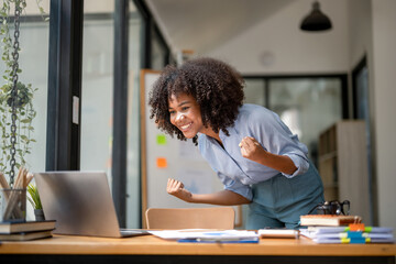 Happy african american woman celebrating victory while receiving good news on her labtop, excited...