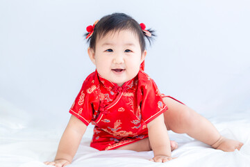 Chinese New Year concept, cute happy little girl in Chinese dress sitting in white living room. Cute Asian baby sitting in white living room, Chinese New Year concept.