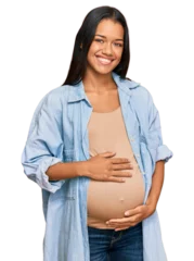 Stoff pro Meter Beautiful hispanic woman expecting a baby showing pregnant belly looking positive and happy standing and smiling with a confident smile showing teeth © Krakenimages.com