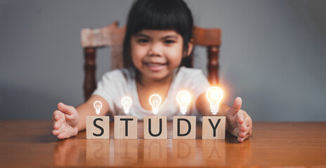 A young girl is holding up a wooden block with the word "study" on it