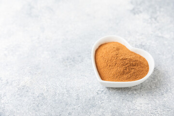 Cinnamon powder in a bowl on a textured wooden background. Spicy spice for baking, desserts and drinks. Fragrant ground cinnamon. Cinnamon stick. Place for text. Copy space.