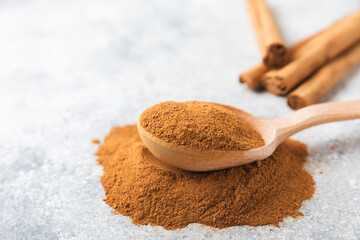 Cinnamon powder in a bowl on a textured wooden background. Spicy spice for baking, desserts and drinks. Fragrant ground cinnamon. Cinnamon stick. Place for text. Copy space.