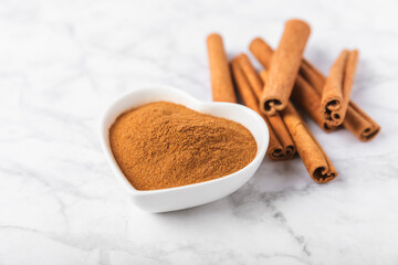 Cinnamon powder in a bowl on a textured wooden background. Spicy spice for baking, desserts and drinks. Fragrant ground cinnamon. Cinnamon stick. Place for text. Copy space.