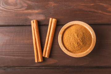 Cinnamon powder in a bowl on a textured wooden background. Spicy spice for baking, desserts and drinks. Fragrant ground cinnamon. Cinnamon stick. Place for text. Copy space.