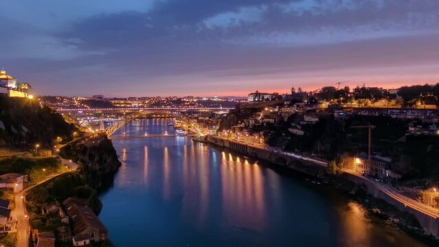 Day to night transition aerial view of the historic city of Porto, Portugal panoramic timelapse with the Dom Luiz bridge. Illuminated waterfront reflected in the river from above