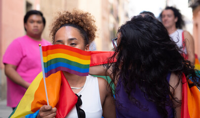 Lesbian girl hiding her face behind rainbow flag in a pride event. LGBTQ community support concept