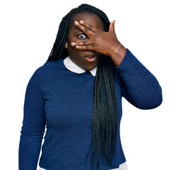 Young black woman with braids wearing casual clothes peeking in shock covering face and eyes with...