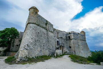 Ancient stone tower stands beside trees and mountains: Fort du Mont Alban, Nice, France