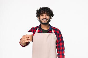 Smiley young Indian bar tender barista holding coffee cup isolated over white background. Hindi man selling serving hot beverages wearing apron