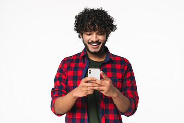 Smiling young Indian man scrolling on the social media in cellphone isolated over white background....