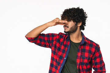 Young Indian man in casual clothes pinching his nose from unpleasant smell isolated over white...