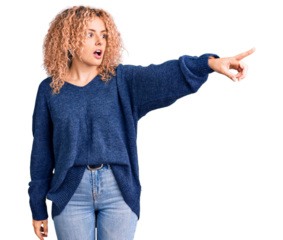 Young blonde woman with curly hair wearing casual winter sweater pointing with finger surprised ahead, open mouth amazed expression, something on the front