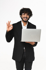 Vertical shot of young Indian businessman using laptop for remote work with okay gesture over white. Isolated portrait of CEO office employee doing online shopping, start up, studying