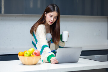 woman relaxing - Happy young teen girl using laptop computer sit at table working learning online in internet at home enjoy morning coffee in cozy house kitchen. Pretty woman wearing sweater at home