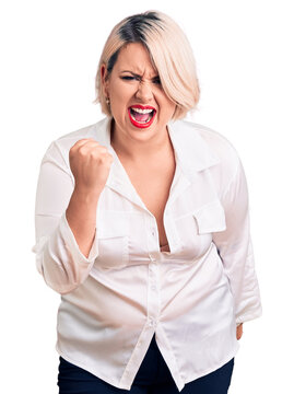 Young blonde plus size woman wearing casual shirt angry and mad raising fist frustrated and furious while shouting with anger. rage and aggressive concept.