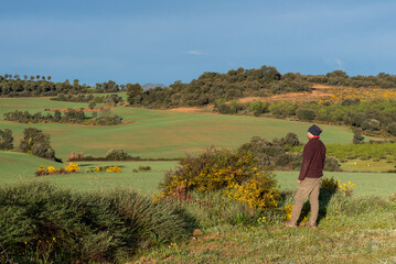 man looking unrecognisable looking at the countryside dressed in mountain clothes, brown trousers, maroon fleece and neckerchief on his head. 