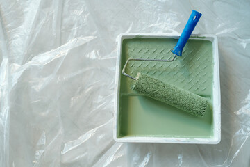 Top view of plastic tray with paintroller and green paint standing on the floor covered with cellophane and prepared for renovation work - 775060561