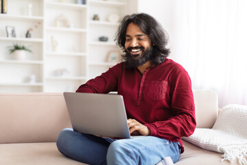 Man laughing while using a laptop on sofa