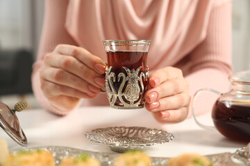 Woman with cup of delicious Turkish tea at white table, closeup