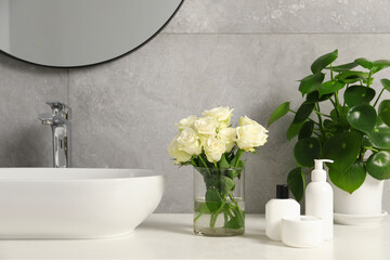 Beautiful roses, houseplant and bath accessories near sink in bathroom