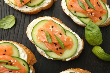 Tasty canapes with salmon, cucumber and cream cheese on board, top view