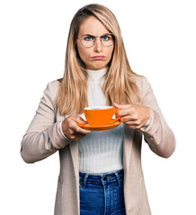 Young blonde woman wearing business style drinking cup of coffee depressed and worry for distress, crying angry and afraid. sad expression.