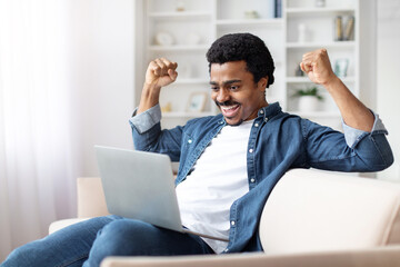 Excited Young Black Man Celebrating Success at Home With Laptop