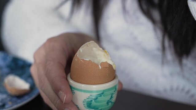 Close-up hand eating Soft-Boiled Egg with cracked top. Protein rich food for breakfast