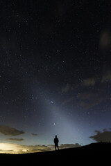 A stargazer looking into the night sky in the middle silhuette showing the zodiacal light in the sky.