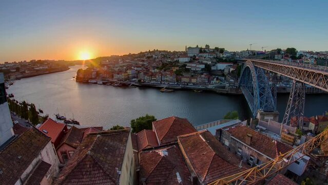 Panorama of old city Porto at river Duoro, with Port transporting boats at sunset timelapse with the Dom Luiz bridge, Oporto, Portugal. Red roofs of historic buildings