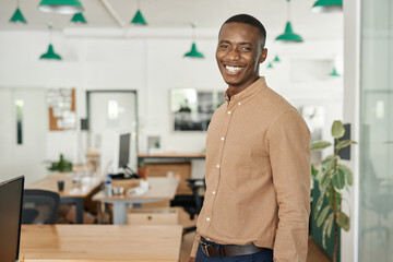 Laughing young African businessman standing alone in an office