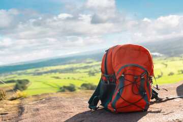 Orange rucksack on top of hill or mountain against blue sky at sunrise. Copy space. Travel concept.