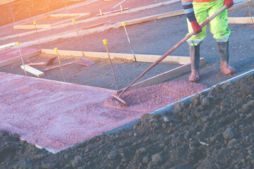 Builders pouring and levelling wet ready-mix concrete into formwork   during new footpath...