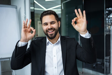 Cheerful man in suit strikes a positive 'ok' sign with hand, confidence and success approve - 775083733